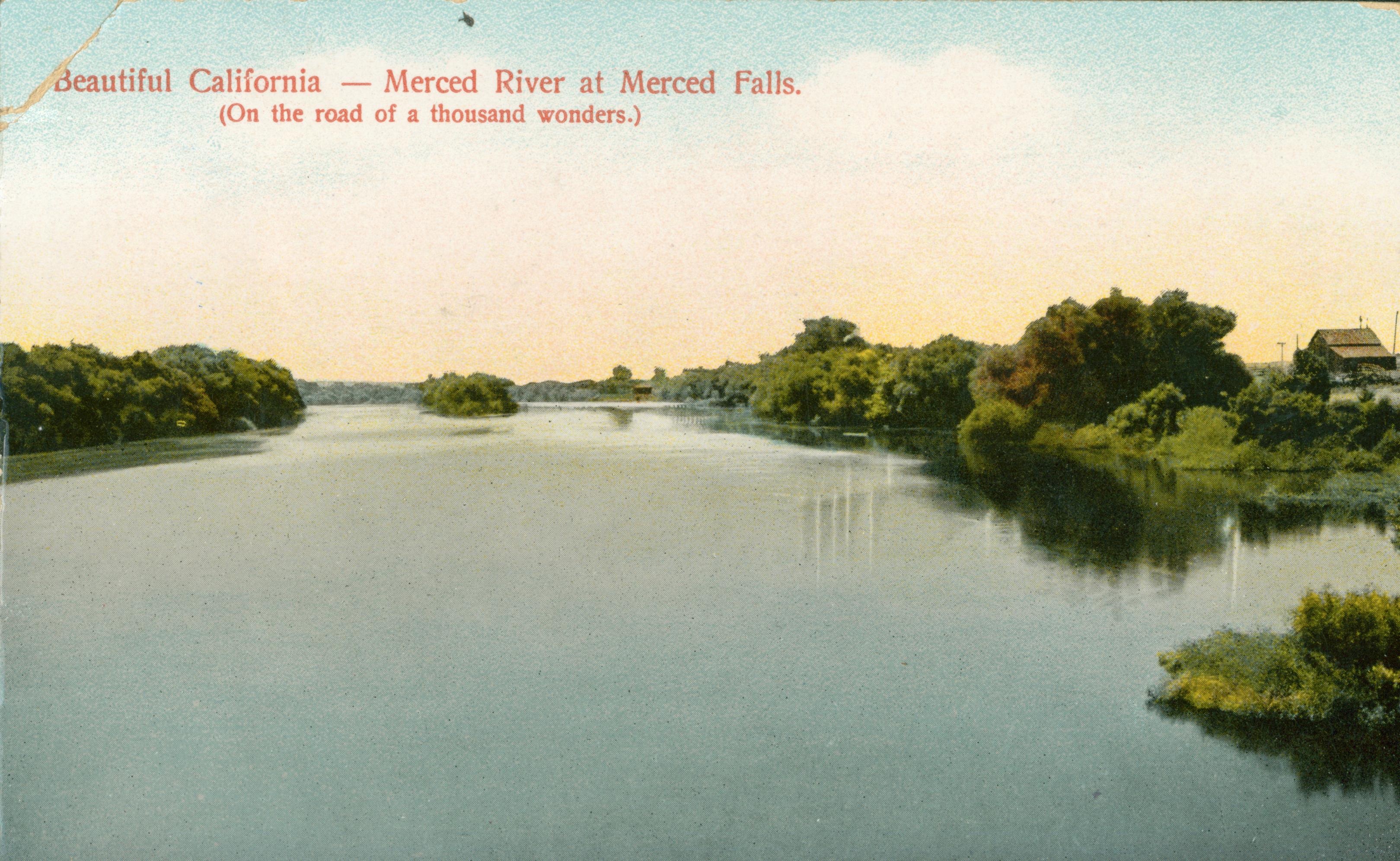 This postcard shows a tree-lined river, with a barn off to the far right.